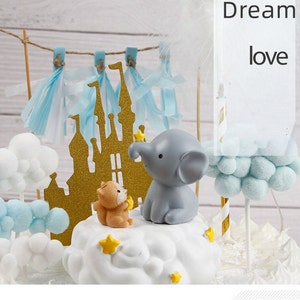 Puede incluir: Un conjunto de adornos para tartas con un castillo dorado, un elefante gris que sostiene una estrella, un zorro marrón que sostiene una estrella y nubes azules y blancas. El texto "Dream love" es visible en el fondo.