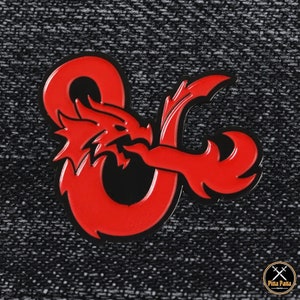May include: A red and black enamel pin featuring the Dungeons & Dragons logo, a dragon intertwined with the letters 'D' and 'D'. The pin has a glossy finish and a black border, set against a textured grey background.