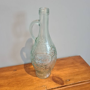 Könnte beinhalten: Eine klare Glasflasche mit Henkel, geprägt mit Trauben und dem Text "Cornish Cider Farm".