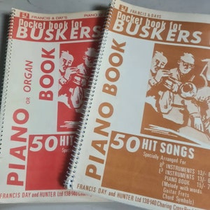 Può includere: Due libri rilegati a spirale intitolati "Pocket book for Buskers" con una copertina rossa e marrone. Il libro a sinistra ha le parole "Piano or Organ" e "50 Hit Songs" sulla copertina. Il libro a destra ha le parole "Piano Book" e "50 Hit Songs" sulla copertina.