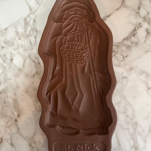 May include: A brown, molded plastic St. Nick figure, holding a basket and staff. The figure is in a long robe and has a long beard. The words "St. Nick" are at the bottom of the figure.