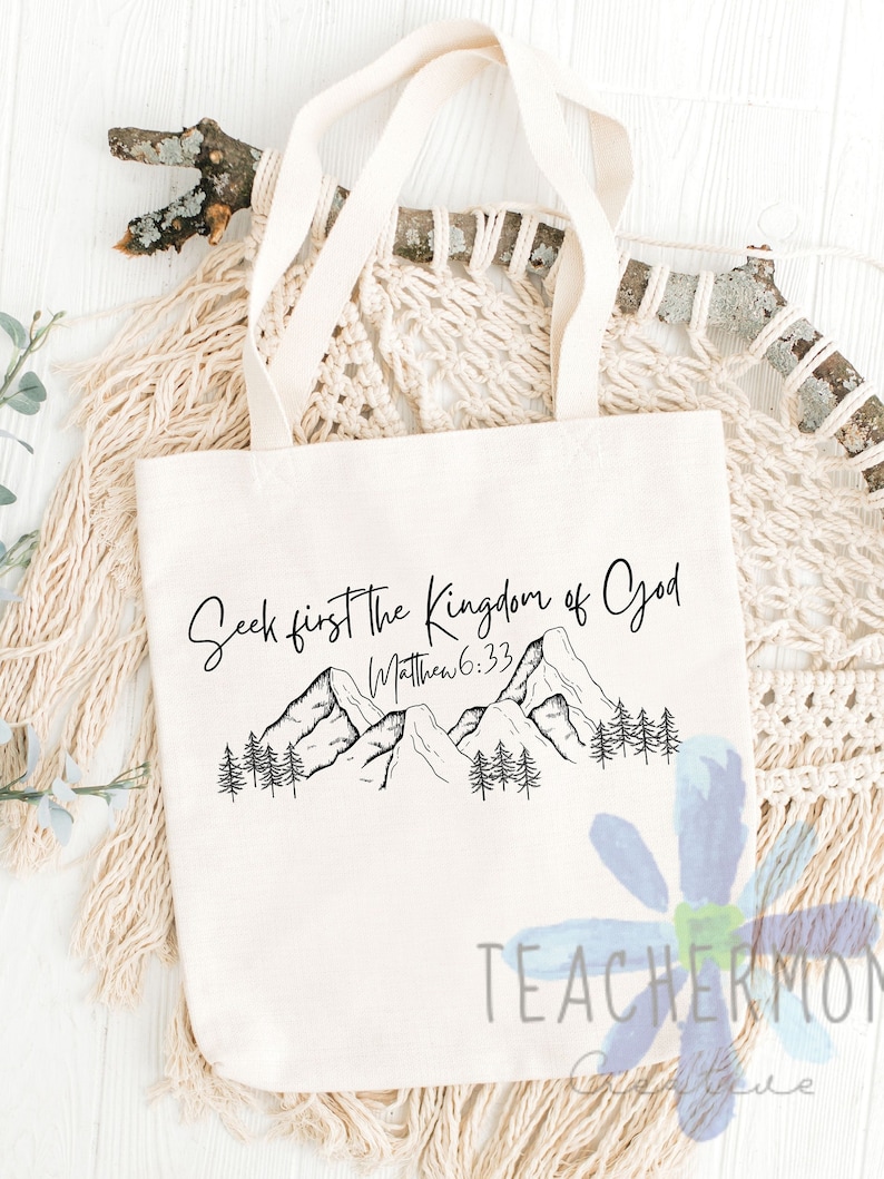 May include: A white canvas tote bag with black text and a mountain scene. The text reads "Seek first the Kingdom of God Matthew 6:33".