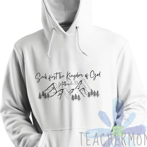 May include: White hoodie with a black graphic of mountains and trees. The text "Seek first the Kingdom of God" is written above the mountains. The text "Matthew 6:33" is written below the mountains.