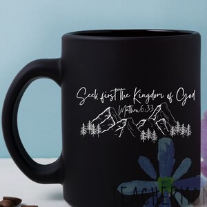 May include: Black ceramic coffee mug with a white design of mountains and trees. The text "Seek first the Kingdom of God" and "Matthew 6:33" is printed on the mug.