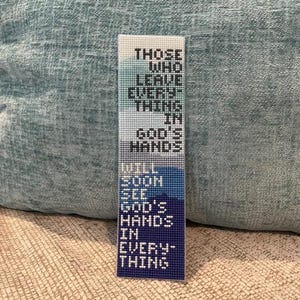 May include: A rectangular cross-stitch bookmark featuring a blue and white gradient background. The text reads: THOSE WHO LEAVE EVERYTHING IN GOD'S HANDS WILL SOON SEE GOD'S HANDS IN EVERYTHING. The design is composed of small, visible grid stitches.