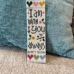 May include: A white cross-stitch bookmark with the words "I am with you always" and the Bible verse "MATT 28 20". The bookmark features hearts, flowers, and a bird design in various colors.