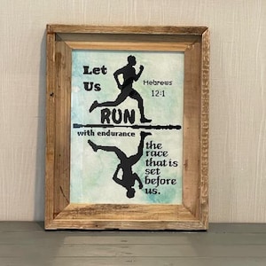 May include: Framed artwork with a rustic wooden frame. The artwork features a silhouette of a runner above a mirrored image of the same runner. Text includes "Let Us RUN with endurance" and "Hebrews 12:1". The background has a watercolor effect.