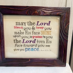 May include: A framed cross-stitch with a religious quote in colorful thread. The quote reads "may the Lord bless you & keep you make His face SHINE upon you, be gracious to you the Lord turn His face toward you AND give you peace. Num 6:21-26"
