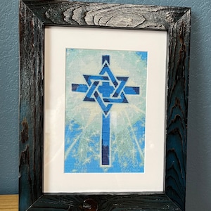 Pode incluir: Obra de arte emoldurada com uma cruz azul sobreposta por uma Estrela de David. A obra de arte está sobre um fundo azul claro com uma borda branca, emoldurada por uma moldura de madeira escura e texturizada.