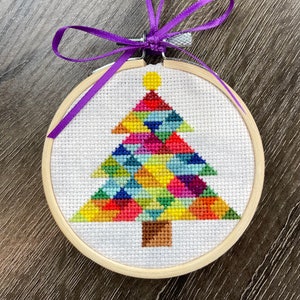 May include: A colorful geometric Christmas tree cross-stitch ornament in a wooden hoop with a purple ribbon.