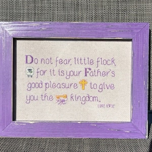 May include: A framed cross-stitch with a purple frame and a white background. The cross-stitch features the text "Do not fear, little flock for it is your Father's good pleasure to give you the kingdom. Luke 12:32".
