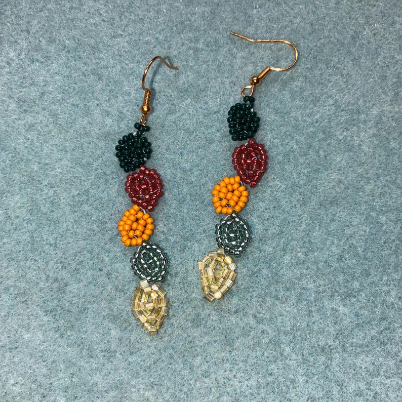 Pu&ograve; includere: Orecchini fatti a mano con perline e ganci dorati. Gli orecchini presentano un design verticale con perline verde scuro, bordeaux, arancione, argento e dorate. Le perline sono disposte a forma di fiore o di foglia.