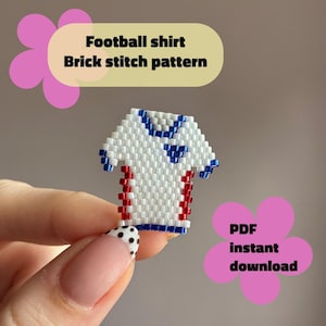 May include: A small beaded football shirt charm created with a brick stitch pattern. The shirt is primarily white with blue accents at the collar and sleeves, and red vertical stripes along the sides. Text reads: Football shirt Brick stitch pattern PDF instant download.