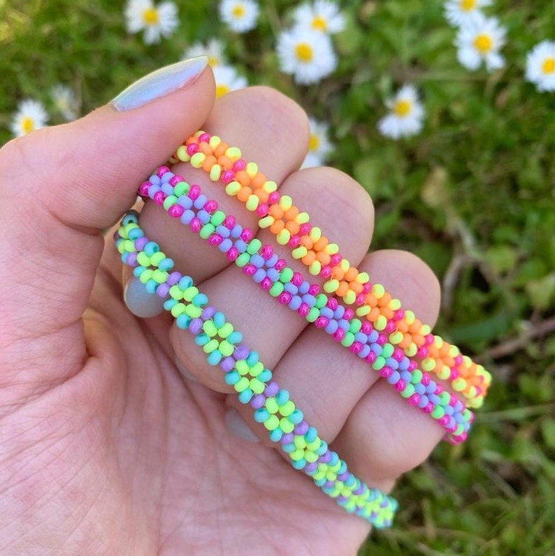 May include: Three colorful beaded bracelets in shades of green, pink, and orange. The bracelets are stacked on top of each other and are made with small, round beads.