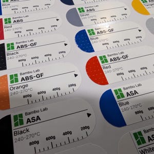 Puede incluir: Una hoja de etiquetas adhesivas rectangulares con extremos redondeados, que presenta el logotipo de Bambu Lab, tipos de materiales como ABS, ABS-GF y ASA, nombres de colores, rangos de temperatura de 240-270&deg;C y escalas de peso de 200g a 800g.