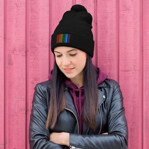 Könnte beinhalten: Eine schwarze Mütze mit einem Regenbogenstreifen-Design. Die Mütze hat einen Bommel oben.