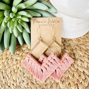 May include: A pair of pink tassel earrings with gold geometric frames. The earrings are handmade and feature a delicate tassel design. The earrings are displayed on a card with the text "Pamela Wehler Handmade Designs".