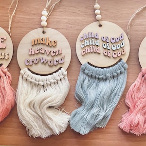May include: Five wooden wall hangings with different phrases. The phrases are "LOVE like Jesus", "make heaven crowded", "child of God child of God child of God", "Praying moms club". Each hanging has a fringe of yarn in a different color: pink, white, light blue, and pink.