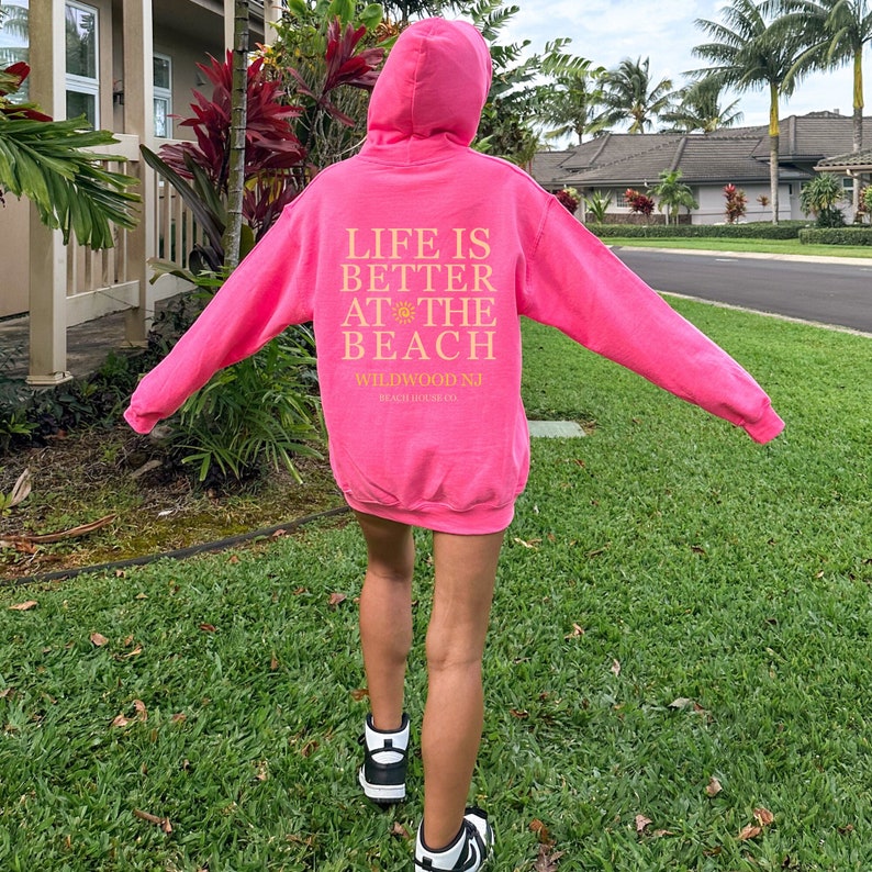 May include: Pink hoodie with the text "Life is better at the beach" and "Wildwood NJ Beach House Co."