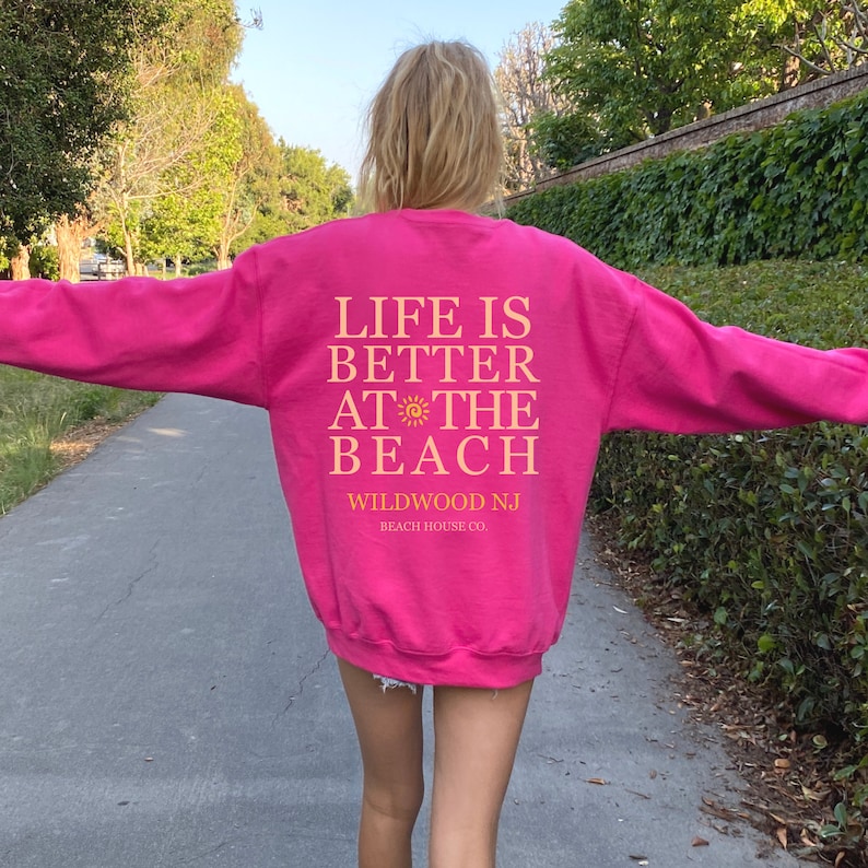 Pu&ograve; includere: Felpa rosa con il testo "Life is better at the beach" e "Wildwood NJ Beach House Co."