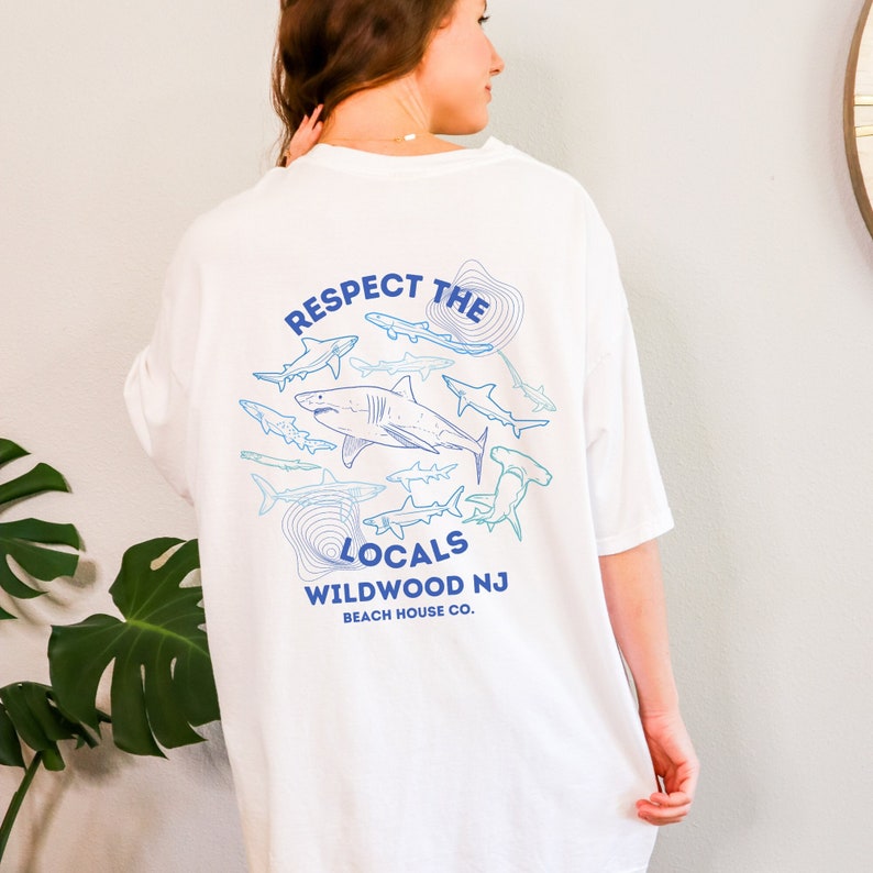 May include: White t-shirt with a blue and white graphic of sharks and the text "Respect the Locals Wildwood NJ Beach House Co."