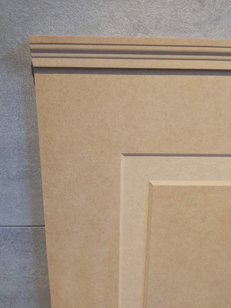 May include: A close-up of a light brown wooden panel with a raised, decorative frame. The panel has a smooth, unfinished surface and is made of medium-density fiberboard (MDF).