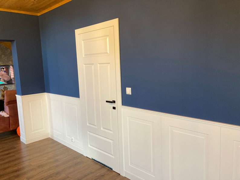 May include: A white door with a black handle is set against a wall with white wainscoting and a dark blue upper wall.
