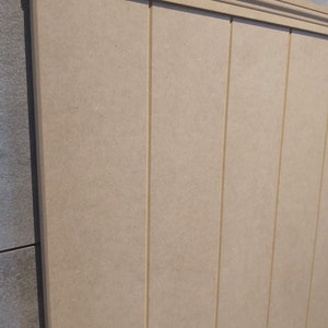 May include: Beige wooden paneling with vertical grooves and a decorative top molding. The paneling has a smooth, uniform surface and is likely used for interior wall decoration or as a design element in a room.