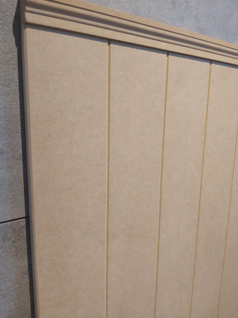 May include: Beige wooden paneling with vertical grooves and a decorative top molding. The paneling has a smooth, uniform surface and is likely used for interior wall decoration or as a design element in a room.