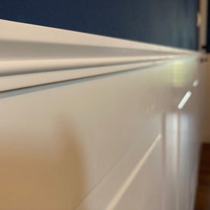 May include: White wainscoting with a white crown molding and a dark blue wall above.