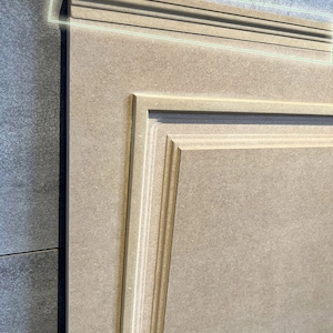 May include: A light brown wooden cabinet door with a raised panel design. The door has a decorative trim around the edge, labeled "LG1".