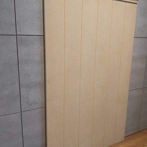 May include: A vertical, rectangular wooden panel with a decorative top molding. The panel is composed of several vertical planks, each with a narrow groove. The wood has a light beige color, and the panel is positioned against a gray tiled wall.