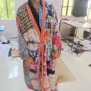 May include: A patchwork robe with a vibrant mix of colors and patterns. The robe features a belt and orange trim with mirrored accents. The text "kurta Bazaar" is visible on the robe. The robe is made of various fabrics.