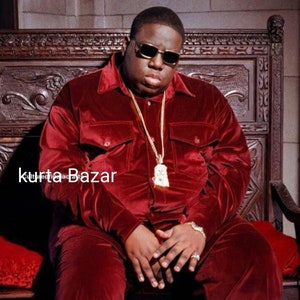 May include: A man wearing a red velvet suit and sunglasses sits on a wooden throne. He is wearing a large gold chain with a pendant.