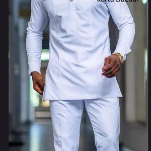 May include: White long-sleeve tunic and matching pants. The tunic has a mandarin collar and button details. The text "kurta Bazaar" is visible on the upper right side of the image. The outfit is a traditional style.