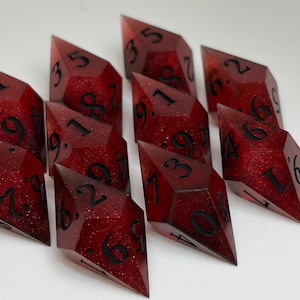 May include: A collection of sharp-edged polyhedral dice in a deep translucent red resin with embedded fine glitter. Each die features elongated diamond-like geometry with black engraved numbers, including various digits like 3, 5, 6, 9, 18, and 29.