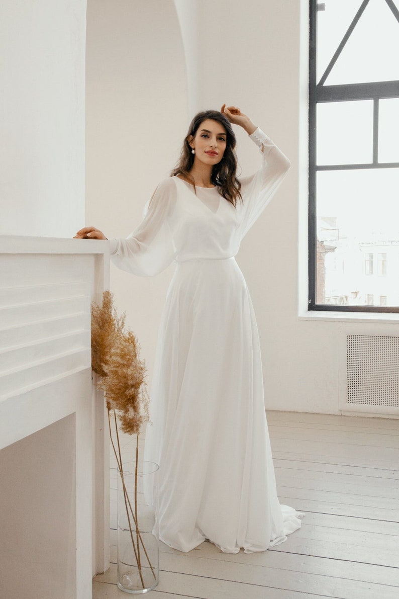 Minimalist chiffon bridal gown with bateau neckline, long sheer sleeves, and soft skirt