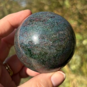 May include: A polished green and pink sphere of Unakite, a metamorphic rock, with swirling patterns and a smooth surface.