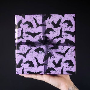 May include: A purple gift box with a black bat pattern and a black ribbon.