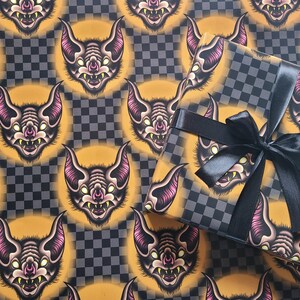 May include: Black and gold wrapping paper with a repeating pattern of cartoon bats. The paper is wrapped around a gift box with a black ribbon.