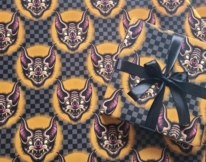 May include: Black and gold wrapping paper with a repeating pattern of cartoon bats. The paper is wrapped around a gift box with a black ribbon.