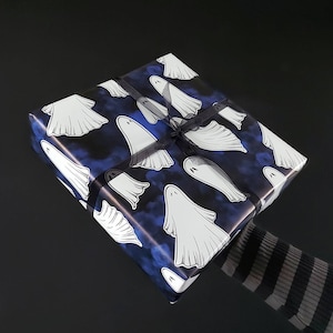 May include: A wrapped gift with a Halloween theme. The wrapping paper is dark blue with white ghost illustrations. A black ribbon is tied around the gift. The background is black.