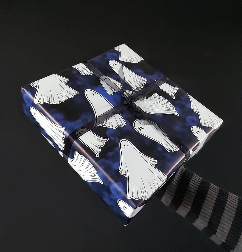 May include: A wrapped gift with a Halloween theme. The wrapping paper is dark blue with white ghost illustrations. A black ribbon is tied around the gift. The background is black.