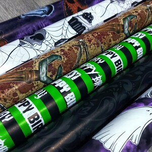 May include: Five rolls of Halloween themed wrapping paper. The designs include a skull and spider web, a rusty tool, a green and black striped pattern with the text "Happy Birthday", a black and white floral pattern, and a purple and white pattern with a ghost.