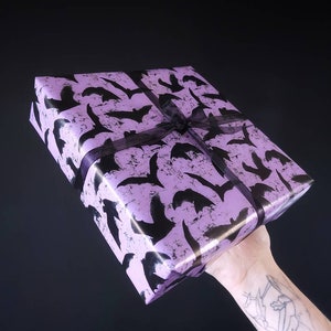May include: A purple gift box with a black bat pattern and a black ribbon.