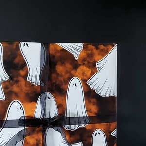 May include: A gift wrapped in orange and black patterned wrapping paper with a black ribbon. The paper features a repeating pattern of white ghosts.