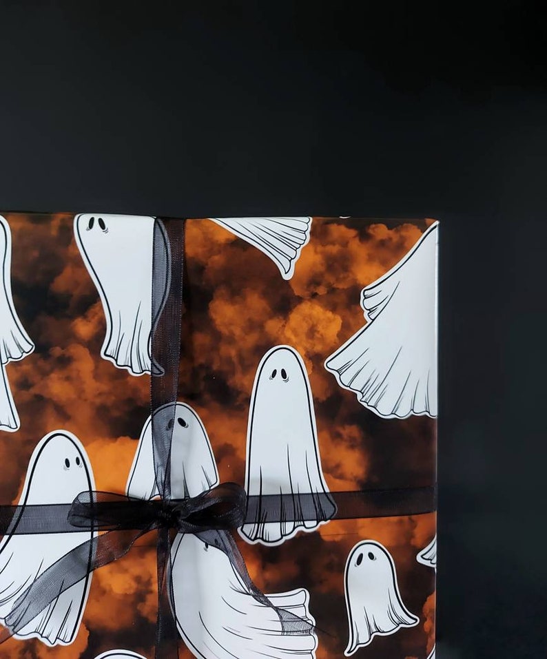 May include: A gift wrapped in orange and black patterned wrapping paper with a black ribbon. The paper features a repeating pattern of white ghosts.