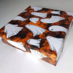 May include: Orange and black wrapping paper with a pattern of white ghosts. The ghosts are in various sizes and positions.