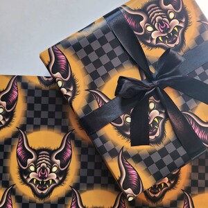 May include: A sheet of yellow and black checkered wrapping paper with a repeating pattern of cartoon bats with pink ears and white eyes. The paper is tied with a black ribbon.
