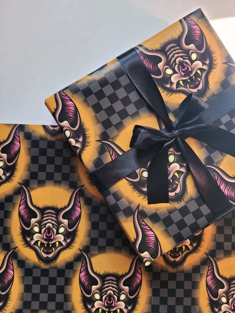 May include: A sheet of yellow and black checkered wrapping paper with a repeating pattern of cartoon bats with pink ears and white eyes. The paper is tied with a black ribbon.